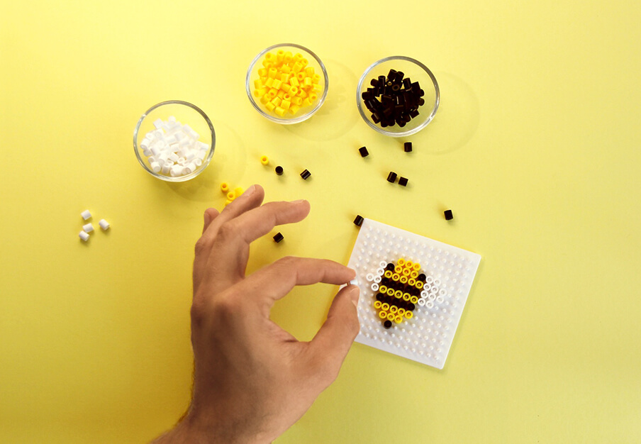 Eine Hand, die eine Biene aus Bügelperlen kreiert